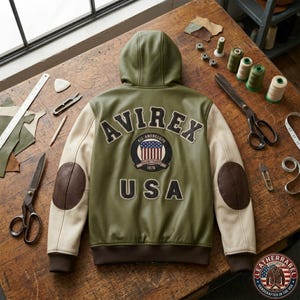May include: An olive green hooded jacket with cream-colored sleeves and dark brown elbow patches. The back features the text AVIREX and USA in black lettering, along with a circular patch displaying an American flag and the text 1976.