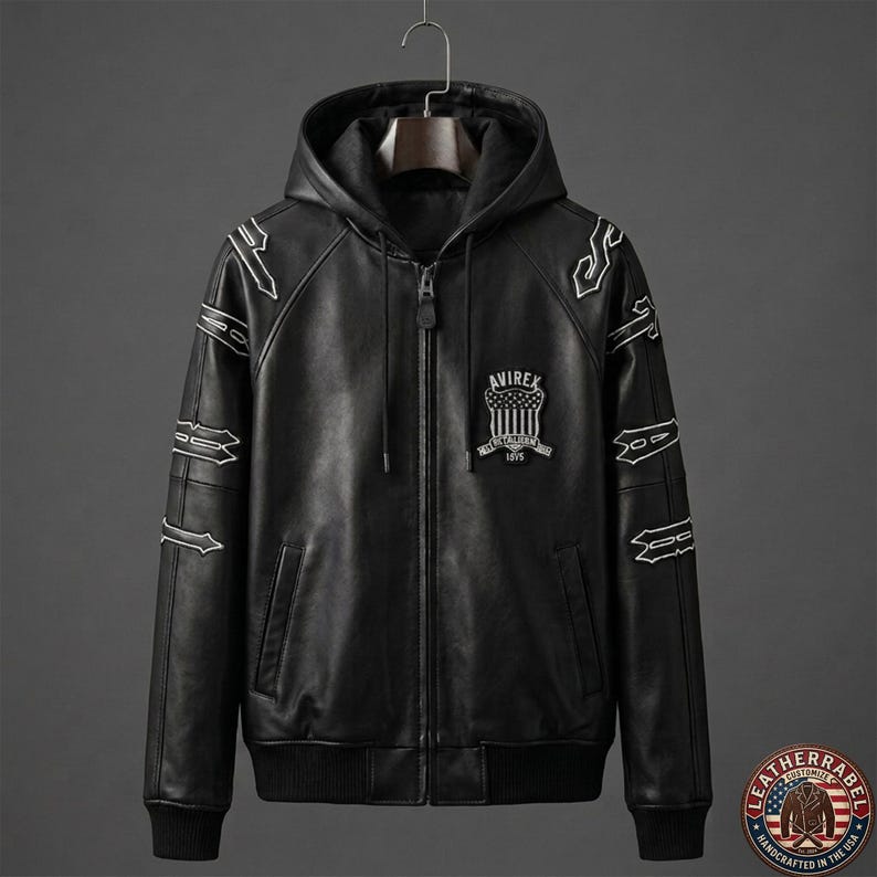May include: Black leather hooded jacket with white embroidered accents and a front zipper. The jacket features the "AVIREX" logo on the chest and is hanging on a hanger. The jacket has a ribbed hem and cuffs.