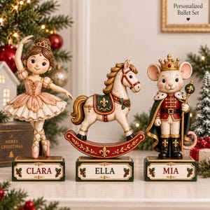May include: Three decorative figurines on rectangular bases labelled Clara, Ella, and Mia. The left is a ballerina in a pink dress, the centre is a rocking horse with a green saddle, and the right is a mouse dressed as a king with a crown and sceptre.