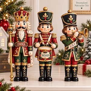Peut inclure: Un trio de figurines casse-noisettes en uniformes rouge, vert et doré. La figurine de gauche porte une couronne et tient un sceptre, marquée EMMA. Celle du centre joue du tambour, marquée NOAH. Celle de droite joue de la trompette, marquée LILY.