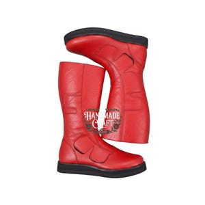 Puede incluir: Un par de botas altas de cuero rojo con suelas negras. Las botas tienen cremallera y cortes decorativos. El texto "HAND MADE CRAFT" está impreso en el lateral de las botas.