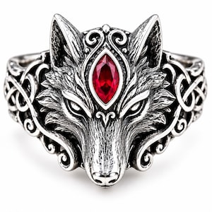 Puede incluir: Un anillo de plata con un diseño detallado de cabeza de lobo y una piedra preciosa roja de corte marquesa situada entre las orejas. La banda está decorada con intrincados patrones de volutas y filigranas que se extienden por los lados.