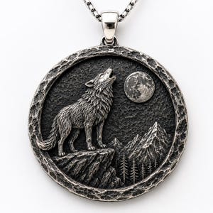 Könnte beinhalten: Ein runder silberner Anhänger mit einem Relief eines Wolfes, der den Vollmond anheult, über einer Bergkette und Tannen. Der Anhänger hat einen strukturierten, gehämmerten Rand und ist mit einer polierten Metallöse an einer Silberkette befestigt.