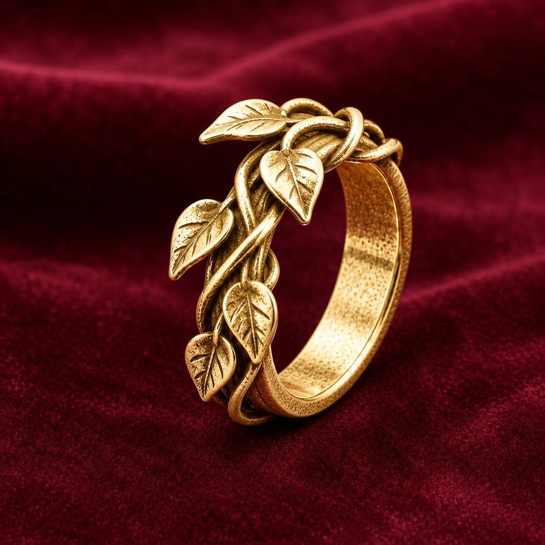 May include: A gold-toned metal ring featuring a textured band designed to resemble intertwined vines. The surface of the ring is adorned with several small, detailed leaf motifs that wrap around the exterior of the band, creating a continuous organic pattern.