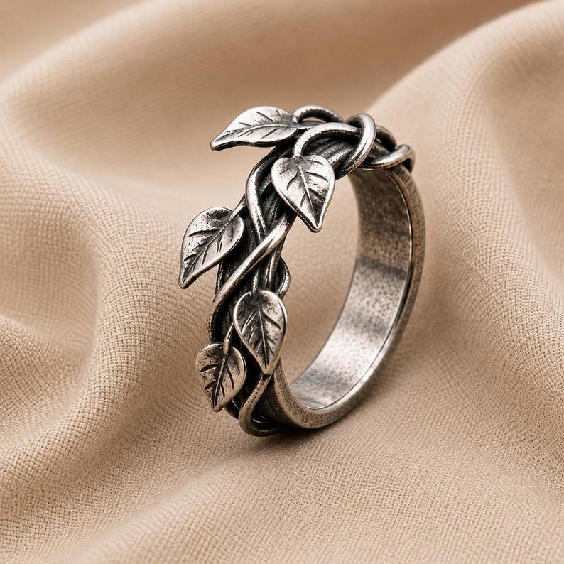 May include: A silver-toned ring featuring a band designed to resemble intertwined vines with multiple small, detailed leaves extending from the surface. The metal has a darkened, oxidized finish that highlights the texture of the leaves and the vine-like structure of the band.