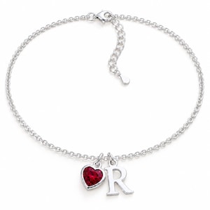 May include: A silver chain anklet featuring a lobster claw clasp and an adjustable extender chain. Two charms hang from the centre: a small, faceted, heart-shaped red gemstone set in a silver frame and a polished silver letter R charm.