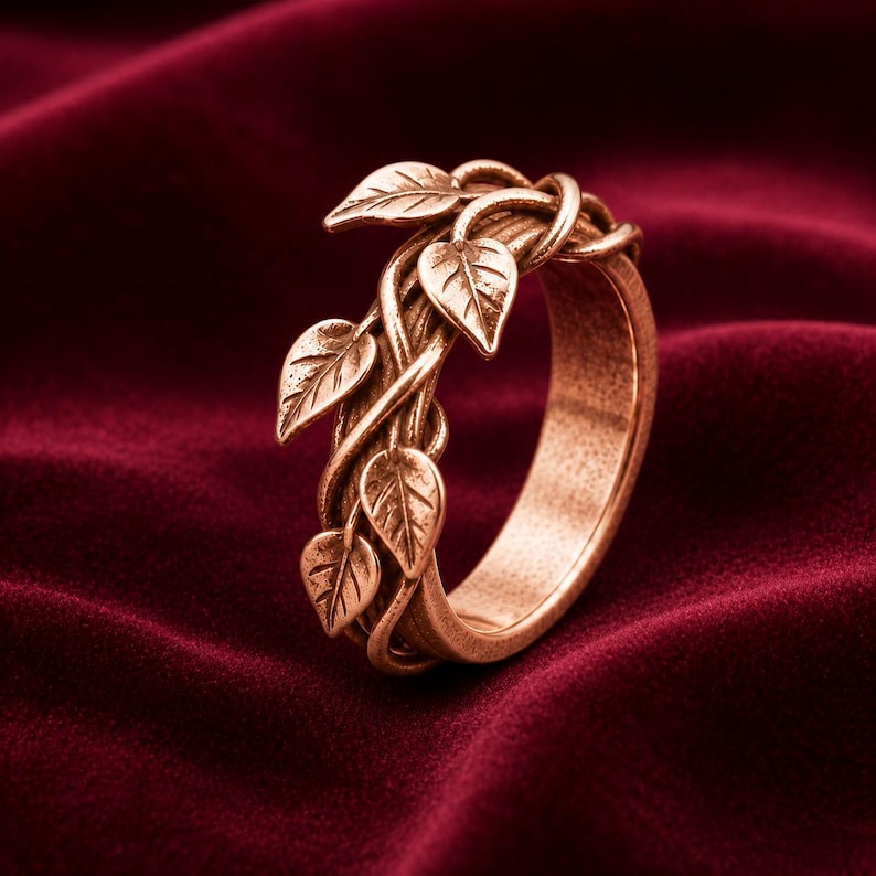 May include: A copper-toned metal ring featuring a band designed to resemble intertwined vines with several small, detailed leaves attached. The surface of the metal has a textured, slightly weathered finish throughout the entire piece.