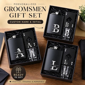 Puede incluir: Juegos de regalo personalizados para padrinos de color negro. Cada juego incluye un frasco, un vaso de chupito y un accesorio con forma de carta de juego, todo presentado en una caja de regalo negra. El texto en la caja dice "PERSONALIZED GROOMSMEN GIFT SET" y "READY TO GIFT".