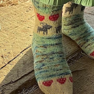 Peut inclure: Paire de chaussettes tricotées beiges, vertes et bleues, avec des fraises rouges et un motif de paysage. Les chaussettes sont portées sur une surface en bois. Accessoire confortable.