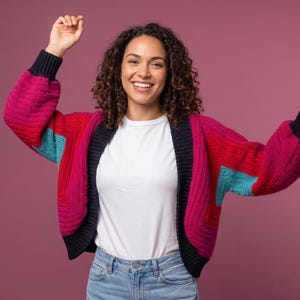 Peut inclure: Un cardigan ouvert aux couleurs vives, avec un motif patchwork. Le pull présente une combinaison de blocs rose vif, rouge et turquoise, avec une bordure bleu marine. Les manches sont longues et le cardigan est fait d'un fil épais et texturé.