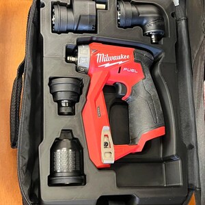 May include: A red and black Milwaukee Fuel cordless installation drill driver set housed in a black molded carrying case. The kit includes the drill body with a belt clip, a right-angle attachment, an offset attachment, and a chuck attachment.