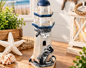 May include: A decorative lighthouse figurine featuring a weathered white wood finish, a dark blue dome top, and blue trim. The structure is adorned with a white seagull emblem, a black anchor wrapped in rope, and a small arched window cutout.