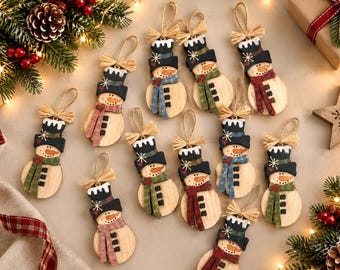 May include: A collection of ten wooden snowman ornaments, each featuring a black top hat with white trim, a painted orange carrot nose, and a fabric scarf in various colors including red, green, and blue, topped with a natural twine hanging loop.