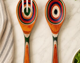 May include: A pair of wooden salad servers featuring a multi-colored, concentric ring pattern in shades of red, orange, green, blue, and natural wood tones. The set includes one slotted spoon and one solid spoon, both with a smooth, polished finish.