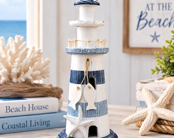 May include: A decorative lighthouse figurine featuring horizontal navy blue and white stripes with a distressed finish. The structure includes a small balcony with rope railing, two hanging wooden fish ornaments, and a white starfish attached to the base.
