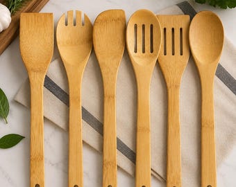 May include: A set of six light brown bamboo kitchen utensils arranged in a row, including a flat spatula, a salad fork, a curved spatula, a slotted spoon, a slotted spatula, and a solid spoon, each featuring a small circular hole in the handle.