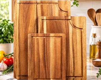 May include: A set of three rectangular wooden cutting boards of varying sizes, each featuring a natural light brown wood grain pattern and a carved juice groove along the perimeter. The boards are arranged in a nested, upright vertical stack.