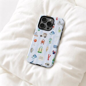 May include: A light blue and white striped phone case featuring small illustrations of a sailboat, a crab, a lobster, a lighthouse, a beach tote, a bicycle, a surfboard-topped vehicle, and the text EAST COAST printed in a small square.