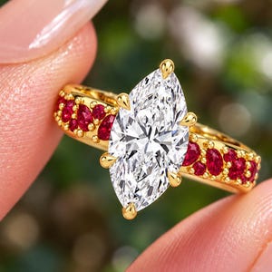 May include: A gold ring featuring a large marquise-cut clear centre stone held by six prongs. The band is accented with multiple small, round, and pear-shaped vibrant red stones set along the sides, creating a detailed and colourful appearance.