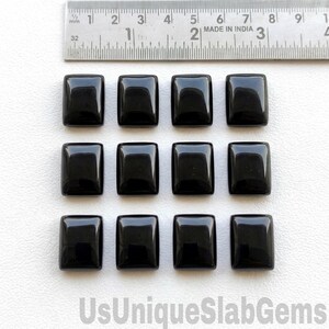 May include: Twelve polished black rectangular gemstones are arranged in a grid. A ruler with millimeter markings is at the top. The gemstones are reflective and have rounded corners. The text "UsUniqueSlabGems" is at the bottom.