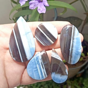 Può includere: Cinque pietre preziose levigate con un motivo a strisce marrone scuro, bianco e azzurro. La collezione comprende una goccia grande, una goccia piccola, un triangolo piccolo, un cerchio e una forma ovale, tutti con una finitura liscia e lucida.