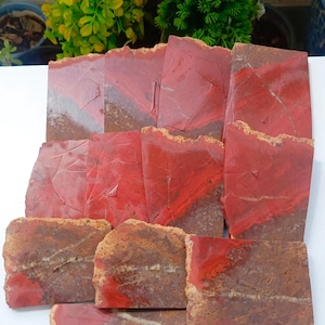 Könnte beinhalten: Eine Sammlung von elf rechteckigen Platten aus rotem und braunem Jaspis-Stein. Jedes Stück weist eine deutliche Farbtrennung auf, mit einem leuchtend roten oberen Bereich und einem strukturierten, erdbraunen unteren Bereich.