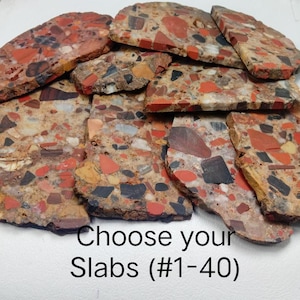 May include: A collection of flat, irregular stone slabs featuring a mosaic-like pattern of red, black, tan, and white mineral fragments embedded in a textured matrix. The image includes the text Choose your Slabs (#1-40) at the bottom.