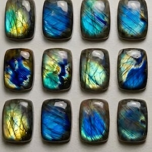 May include: Twelve rectangular labradorite gemstones with iridescent blue, green, and yellow flashes. Each stone has a polished surface and a unique pattern of color variations. The stones are arranged in a grid.