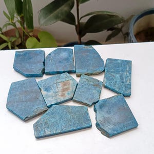 Puede incluir: Una colección de nueve losas de piedra apatita azul, planas y de formas irregulares. Cada pieza presenta un color azul vibrante y saturado con vetas naturales visibles, superficies texturizadas y bordes rugosos sin pulir.