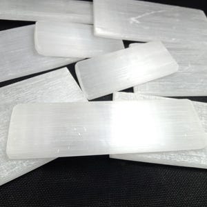 May include: A collection of rectangular selenite slabs with a translucent, fibrous white appearance. Each piece features a smooth, flat surface with a subtle pearlescent sheen, arranged in an overlapping pattern to display their natural texture.