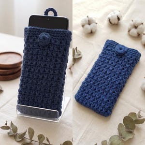 May include: A dark blue crochet phone pouch featuring a textured stitch pattern, a small circular loop at the top, and a matching circular button closure. The pouch is shown holding a smartphone in one view and lying flat in another view.
