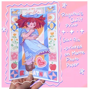 Puede incluir: Una impresión de Ragatha's Quilt, con una ilustración de muñeca con un vestido azul y pelo rojo. La impresión mide 15,24 x 22,86 cm y está impresa en papel fotográfico mate. La obra tiene un borde rosa y la palabra "smile".