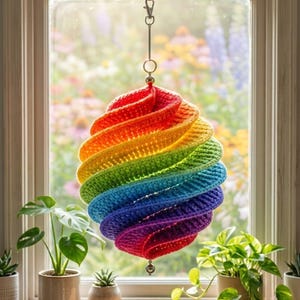 May include: A hanging crochet ornament featuring a spiral, multi-colored rainbow design. The object is constructed with red, orange, yellow, green, blue, indigo, and violet yarn. It is suspended from a silver-toned metal ring and a lobster clasp.