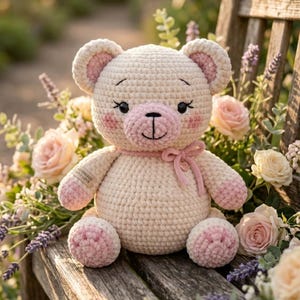 May include: A handmade crochet teddy bear in cream with pink accents on the ears, paws, and snout. The bear has a pink ribbon around its neck and is sitting on a wooden bench surrounded by roses and lavender.