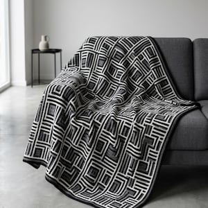 May include: A black, white, and gray geometric patterned blanket draped over a gray sofa. The blanket features a repeating rectangular design with a dark border. The blanket adds a modern touch to the living room.