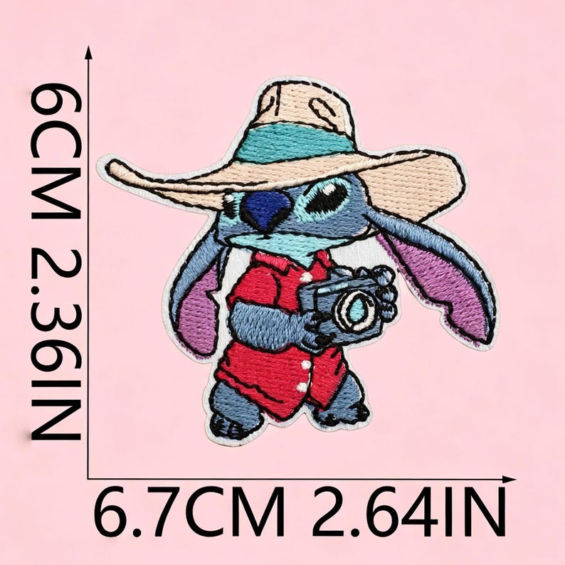 Puede incluir: Un parche bordado que muestra un personaje azul con un sombrero beige con una banda turquesa y una camisa roja, sosteniendo una c&aacute;mara. El parche mide 6 cm por 6,7 cm, o 2,36 pulgadas por 2,64 pulgadas, seg&uacute;n las l&iacute;neas de medici&oacute;n.