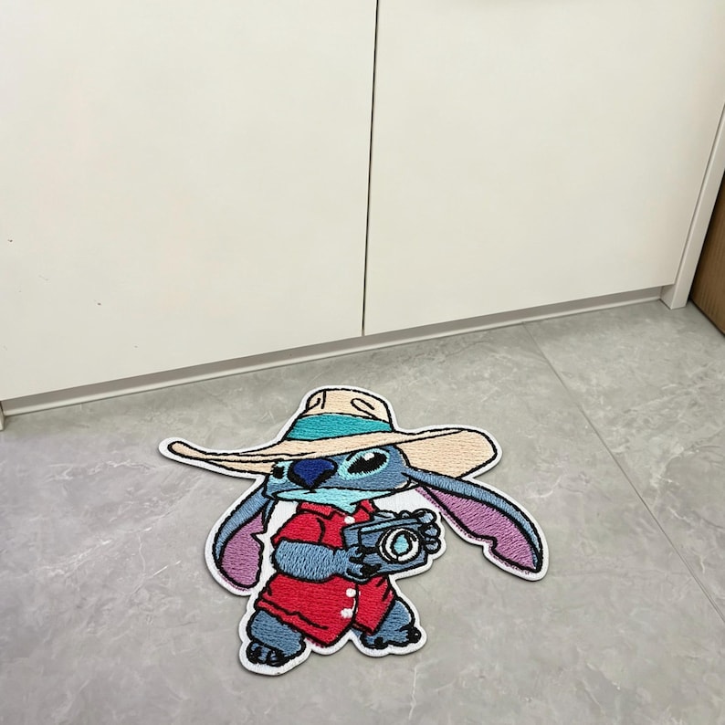 Puede incluir: Un parche bordado azul que muestra a un personaje con un sombrero beige de ala ancha con una banda turquesa, una camisa roja de botones y sosteniendo una c&aacute;mara. El personaje tiene orejas grandes, una nariz azul oscuro y pecho azul claro.