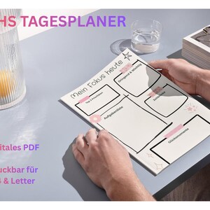 Könnte beinhalten: Ein weißer Planer mit schwarzen Umrissen und dem Text "Mein Fokus heute" wird von einer Person gehalten. Der Planer hat Abschnitte für Aufgaben und Notizen. Die Wörter "Digital PDF" und "Druckbar für A4 & Letter" sind ebenfalls sichtbar.