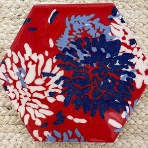 Könnte beinhalten: Sechseckige Fliese mit glänzendem rotem Hintergrund und einem Blumenmuster in Weiß, Hellblau und Marineblau. Das Design der Fliese zeigt ein stilisiertes Blumenmotiv und schafft ein dekoratives Element.