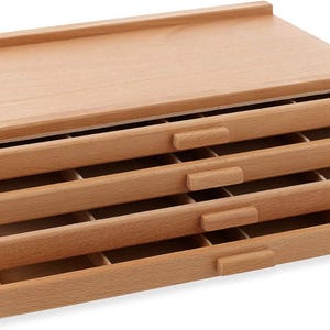 Puede incluir: Una caja de almacenamiento de madera de color claro con cuatro cajones extraíbles. Los cajones están divididos en pequeños compartimentos. La parte superior de la caja tiene un borde elevado. La caja tiene el texto "760/605" impreso.
