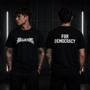 May include: Black t-shirts with white text. One shirt says "HellDivers" in a stylized font. The other shirt says "FOR DEMOCRACY". The shirts are worn by a person in a dark setting.