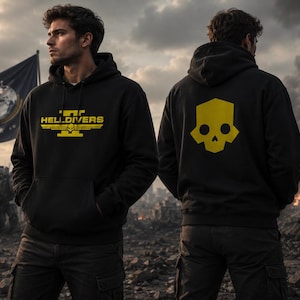 Könnte beinhalten: Schwarzer Kapuzenpullover mit gelbem "HELLDIVERS"-Schriftzug auf der Vorderseite und einem gelben Totenkopf-Design auf der Rückseite. Die Person trägt den Hoodie in einer zerstörten Umgebung.