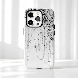 May include: A white smartphone case featuring a black ink-style illustration of a mandala pattern in the upper corner with delicate hanging chains, beads, and leaf-shaped charms extending downwards across the surface of the protective cover.