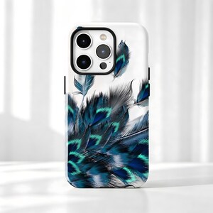 May include: A white smartphone case featuring a detailed graphic print of layered peacock feathers in shades of deep navy blue, royal blue, and vibrant teal. The design covers the back of the case, extending around the camera lens cutout area.