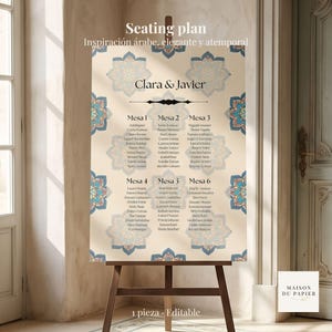 Puede incluir: Un plano de asientos beige con un diseño floral en azul y turquesa, exhibido en un caballete de madera. El plano incluye los nombres de los invitados y las mesas, con los nombres "Clara & Javier" en la parte superior. El texto en la parte inferior dice "1 pieza. Editable".