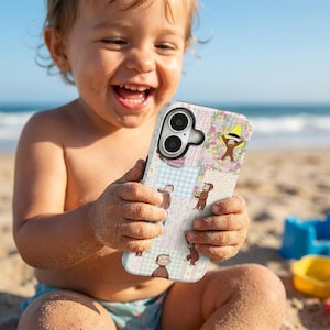 May include: A patterned phone case with illustrations of a monkey in different poses. The case has a patchwork design with a white background and pink, blue, and beige squares. The phone is held by a child on a sandy beach.