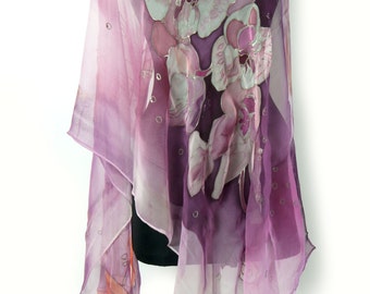 May include: A purple and pink silk scarf with a hand-painted design of orchids. The scarf is draped over a mannequin and has a light, flowing texture.