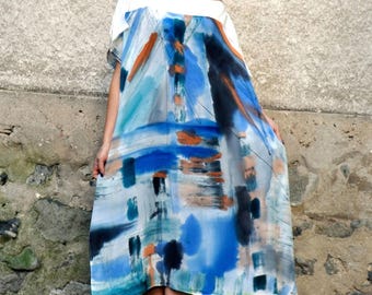Puede incluir: Una mujer con un vestido maxi de estampado abstracto blanco y azul con zapatos blancos. El vestido tiene un corte holgado y una silueta fluida.