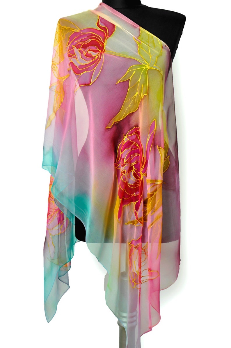 May include: A sheer silk scarf with a colorful ombre design featuring pink, yellow, and blue hues. The scarf is decorated with hand-painted floral motifs in shades of pink and gold.