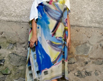 May include: A woman wearing a white top and a long, flowing dress with a colorful abstract print. The dress has a loose, flowing fit and features shades of blue, yellow, and purple.